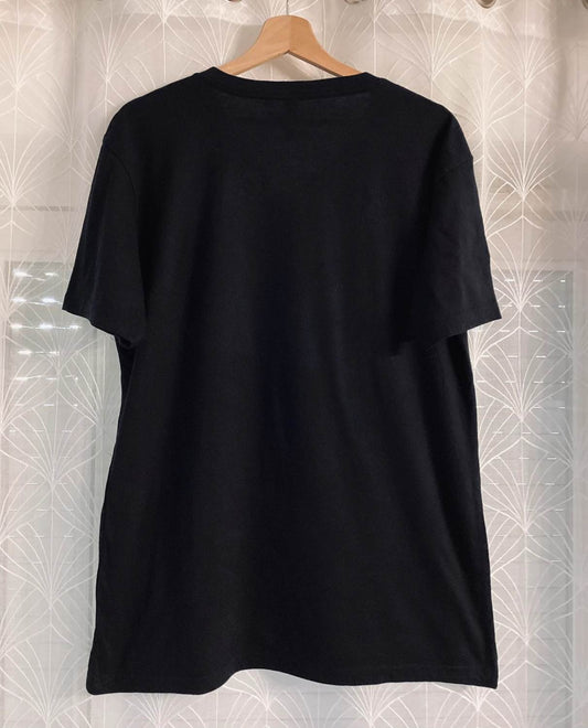 T-shirt noir oversize en coton, vue dos, suspendu sur cintre en bois, fond rideau motif géométrique